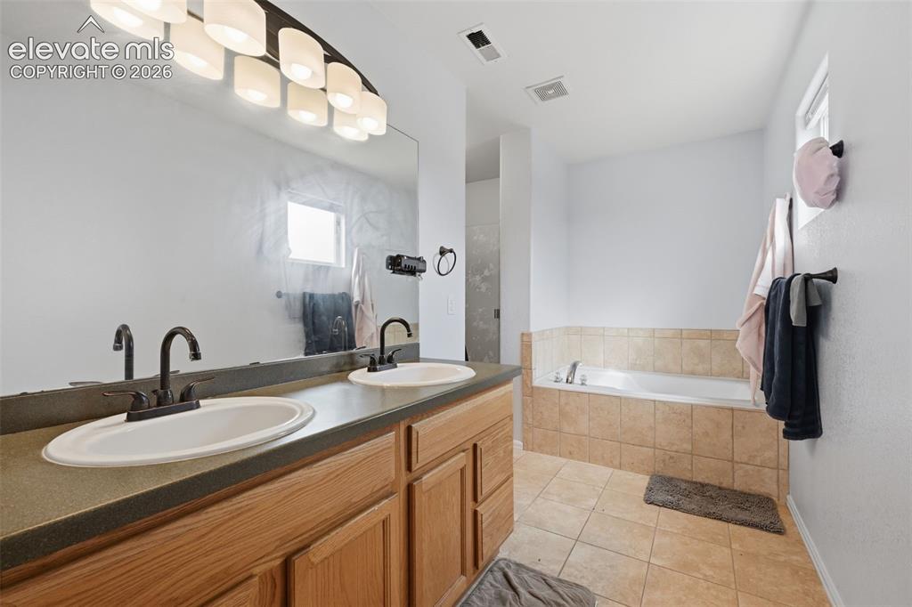 Image 16 of 21: Dual vanity with wood-finish cabinetry, a drop-in soaking tub with tiled su