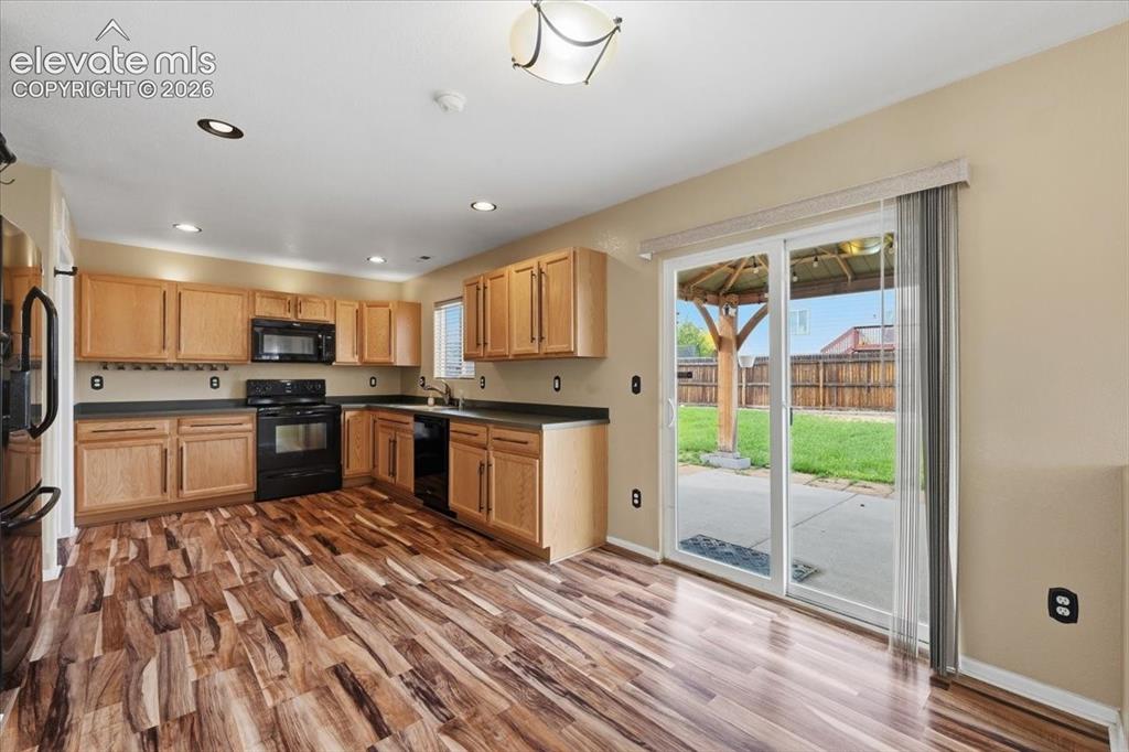 Image 9 of 26: Kitchen featuring wood-finish flooring, light wood cabinetry, black applian