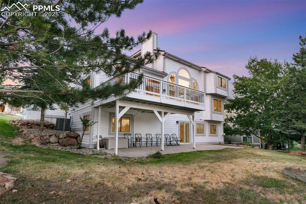 Image 5 of 50: View of front of house with a patio area, a chimney, a lawn, and a balcony