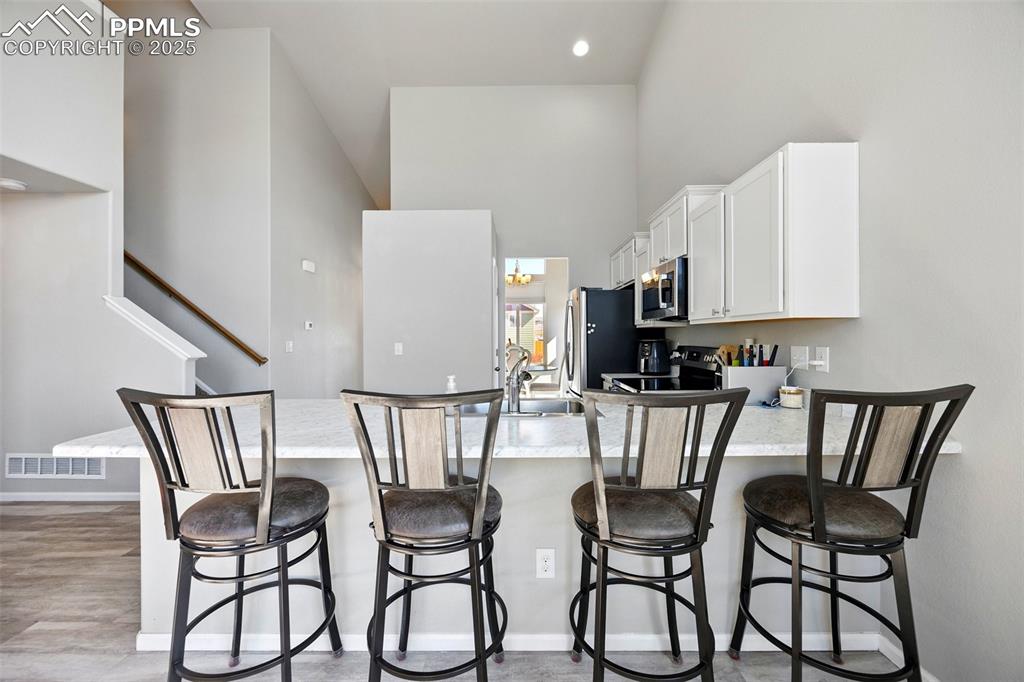 Image 11 of 46: Kitchen featuring a peninsula, white cabinets, a high ceiling, a breakfast