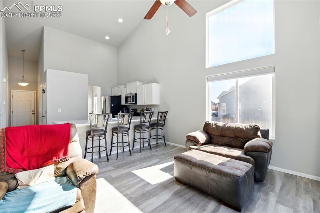 Image 2 of 46: Living area with a high ceiling, light wood-style flooring, ceiling fan, he