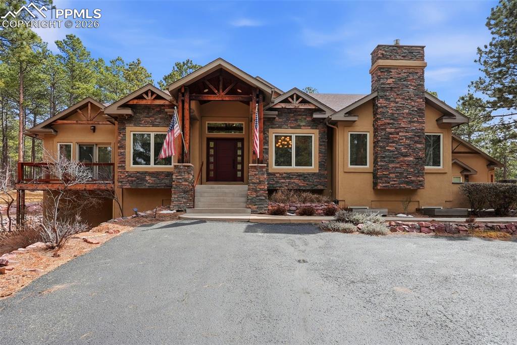 Caption: View of front with of home stone siding, stucco siding, a chimney, and martini balcony