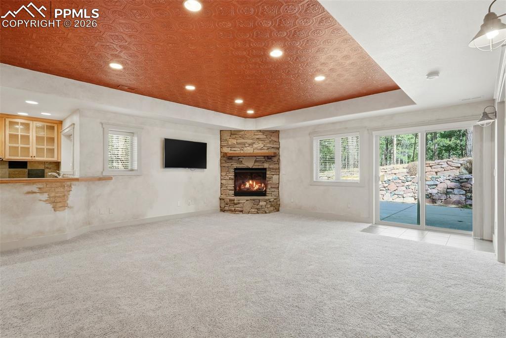 Image 37 of 50: Family Room with a tray ceiling, carpet floors, and a stone fireplace