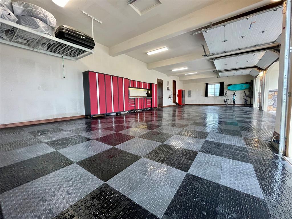 Image 45 of 50: Expansive four-car garage with upgraded flooring, organized storage, and br