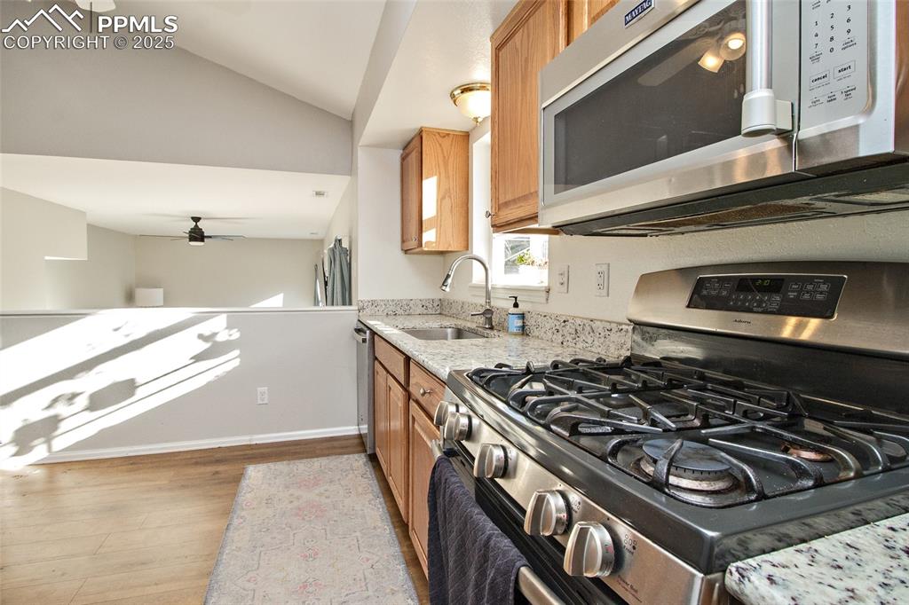 Image 21 of 43: Kitchen featuring stainless steel appliances, light stone counters, vaulted