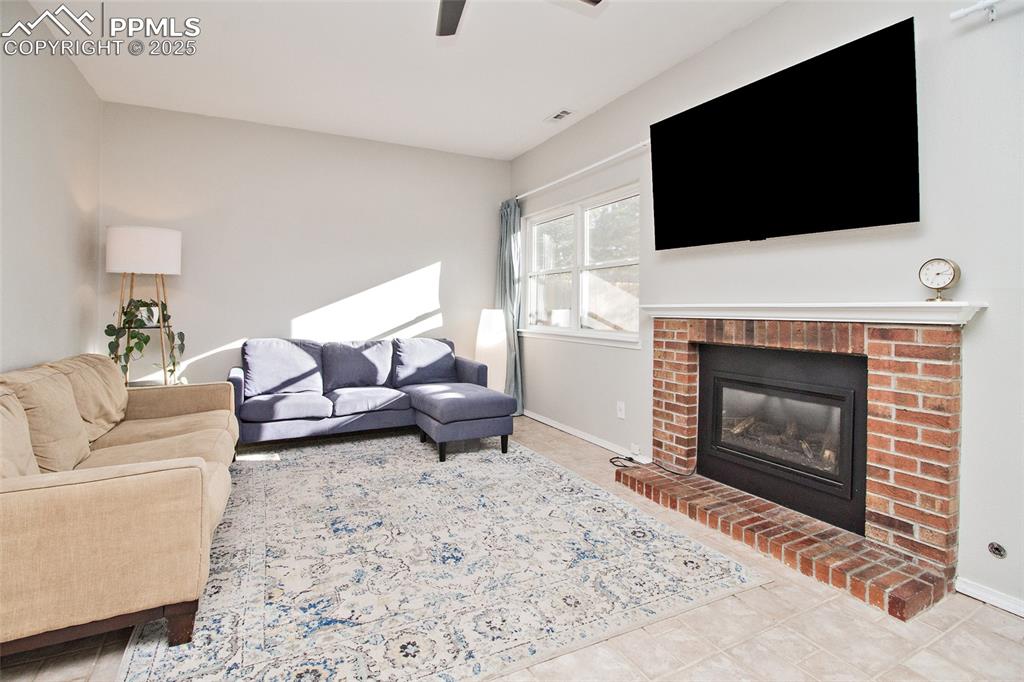 Image 26 of 43: Living room with a fireplace, ceiling fan, and light tile patterned floorin