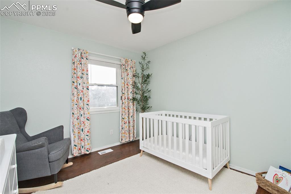 Image 39 of 43: Bedroom featuring a crib, wood finished floors, and a ceiling fan