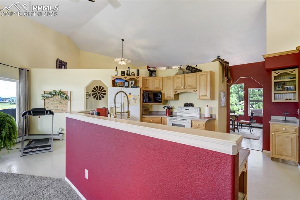 Image 10 of 50: Kitchen with light brown cabinets, white appliances, lofted ceiling, light 