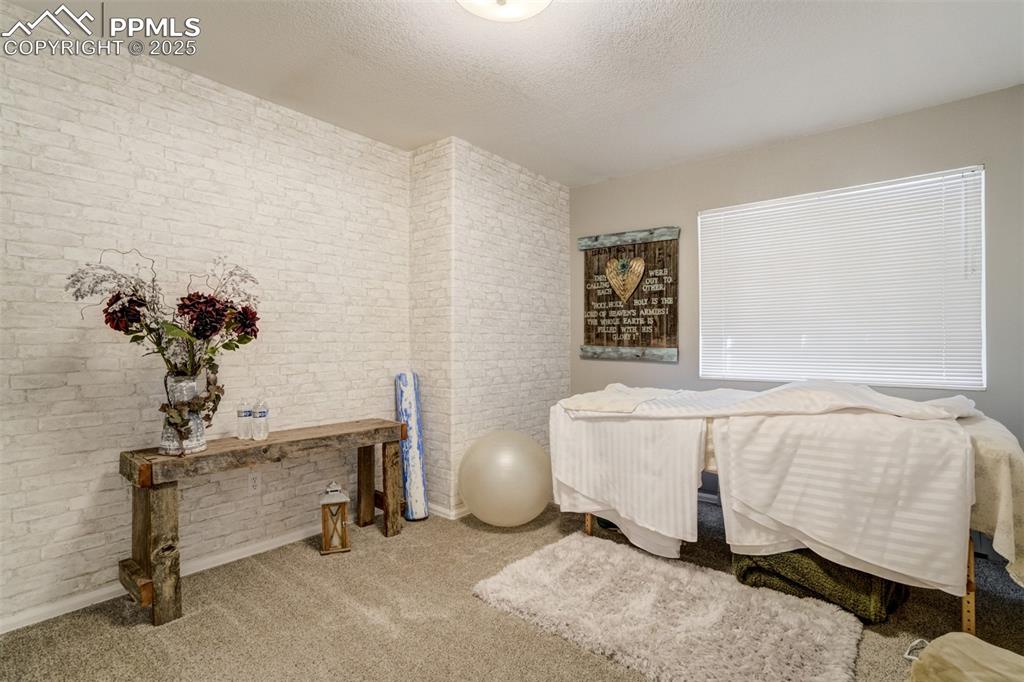 Image 31 of 50: Carpeted bedroom featuring a textured ceiling and brick wall