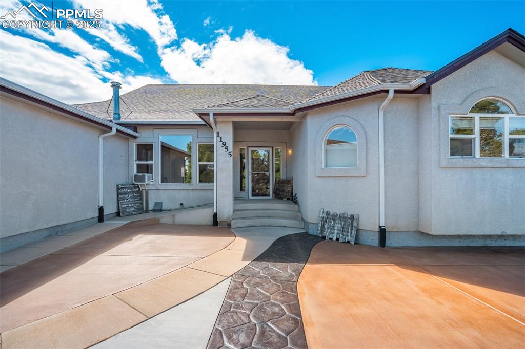 Image 4 of 50: Doorway to property featuring stucco siding and a shingled roof