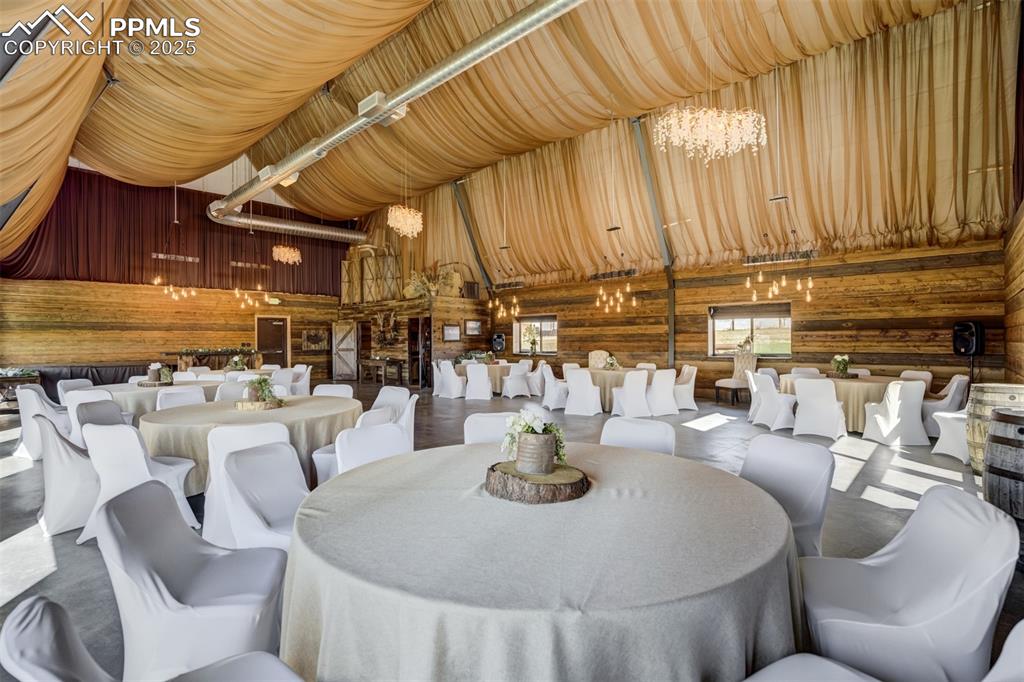 Image 46 of 50: Dining space with a chandelier, a towering ceiling, wooden walls, and concr