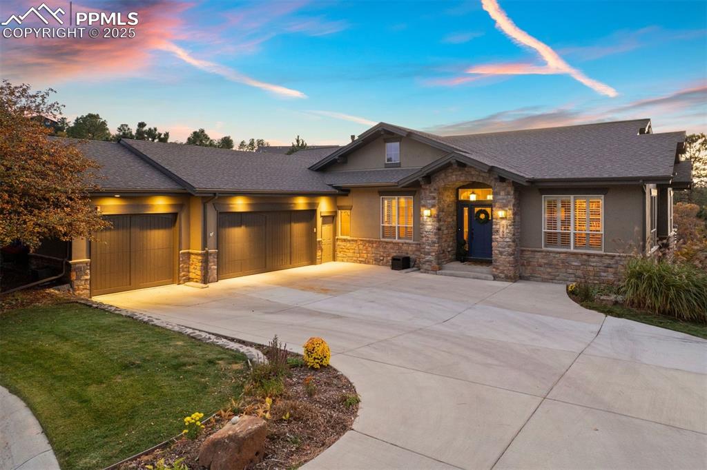 Caption: View of front of property with stone siding, driveway, an attached garage, and roof with shingles
