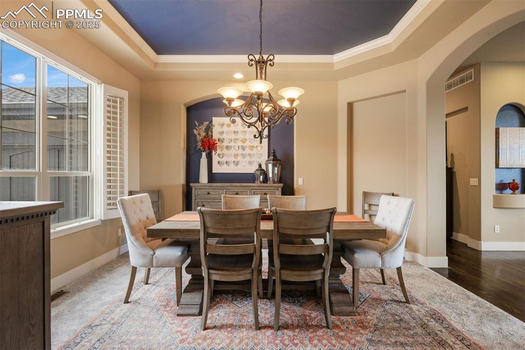 Image 12 of 50: Dining space with arched walkways, a raised ceiling, and a chandelier