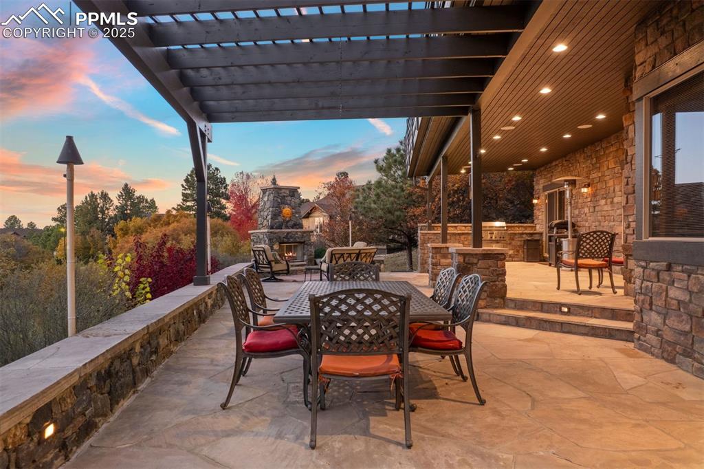Image 28 of 50: Patio terrace at dusk with an outdoor stone fireplace, outdoor dining space