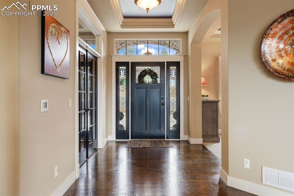 Image 3 of 50: Entryway with a raised ceiling, dark wood-type flooring, and arched walkway