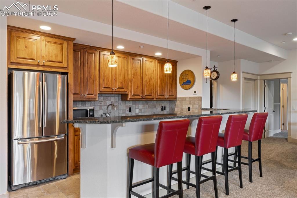 Image 34 of 50: Kitchen with brown cabinetry, stainless steel appliances, a breakfast bar, 