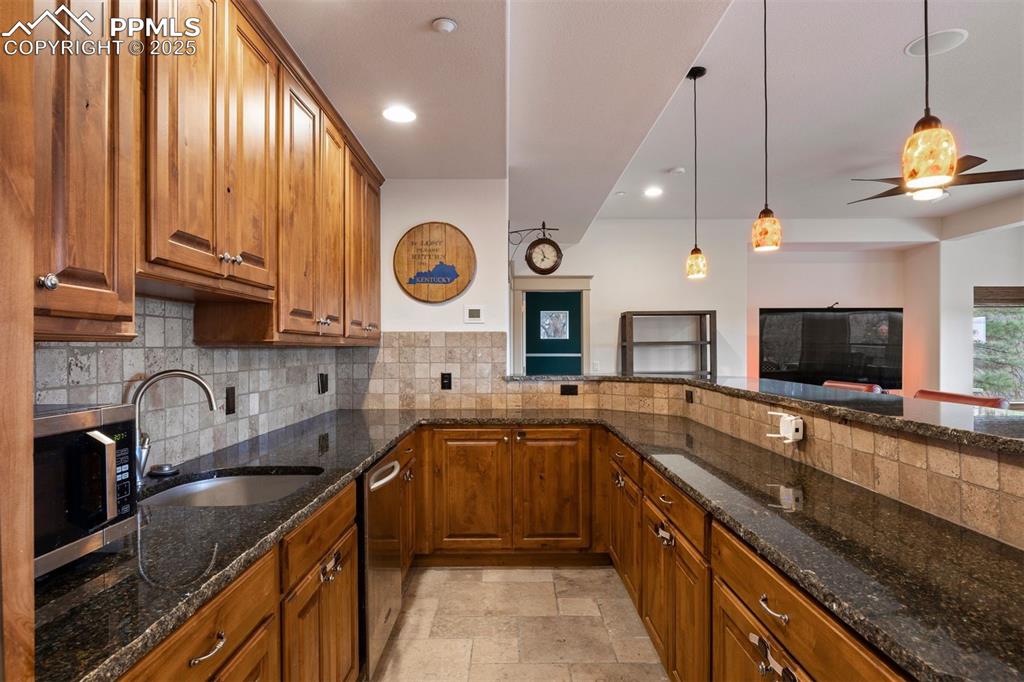Image 35 of 50: Kitchen featuring dark stone counters, brown cabinets, stainless steel appl