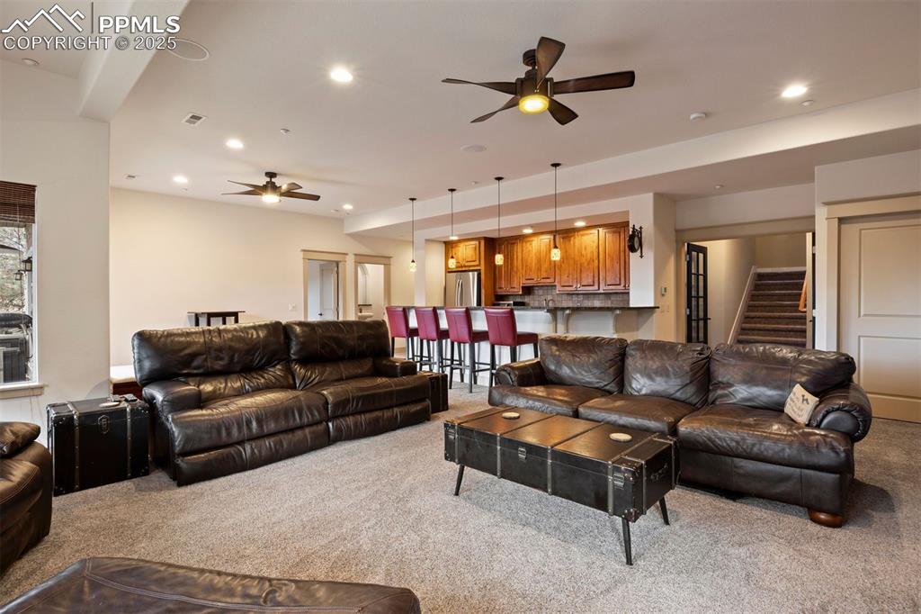 Image 36 of 50: Carpeted living area featuring a ceiling fan, stairs, and recessed lighting