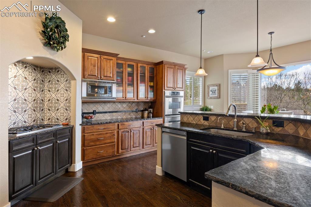 Image 4 of 50: Kitchen featuring glass insert cabinets, backsplash, brown cabinetry, dark 