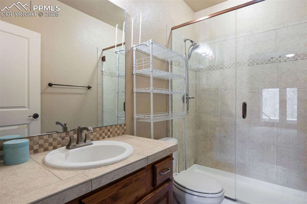 Image 43 of 50: Bathroom with vanity, a stall shower, a textured wall, and backsplash