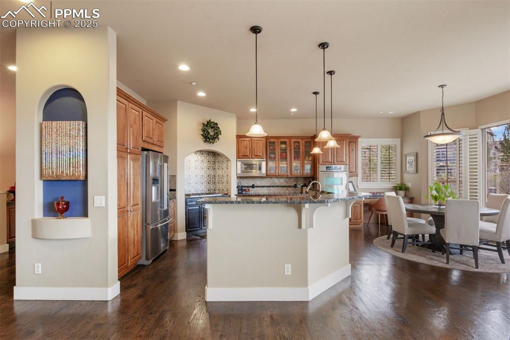 Image 9 of 50: Kitchen with tasteful backsplash, brown cabinets, glass insert cabinets, a 
