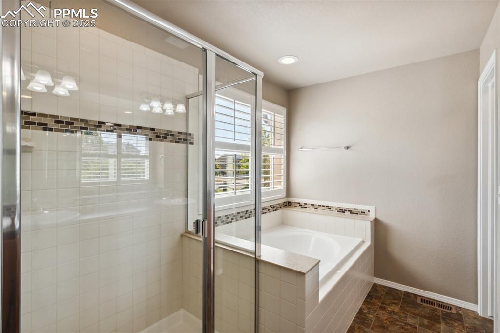 Image 16 of 50: Bathroom featuring a shower stall, a bath, baseboards, and stone finish flo