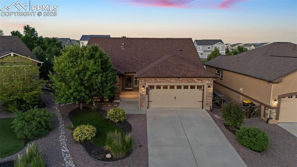 Image 2 of 50: View of front of home with driveway, a garage, a shingled roof, stone sidin