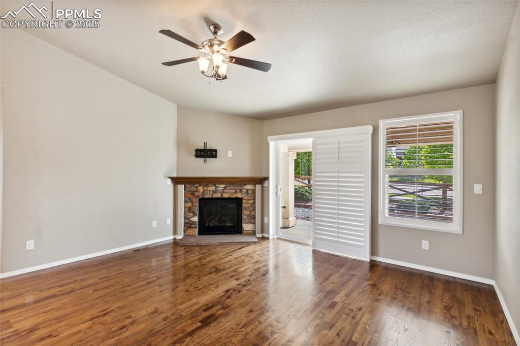 Image 21 of 50: Unfurnished living room with ceiling fan, wood finished floors, and a stone