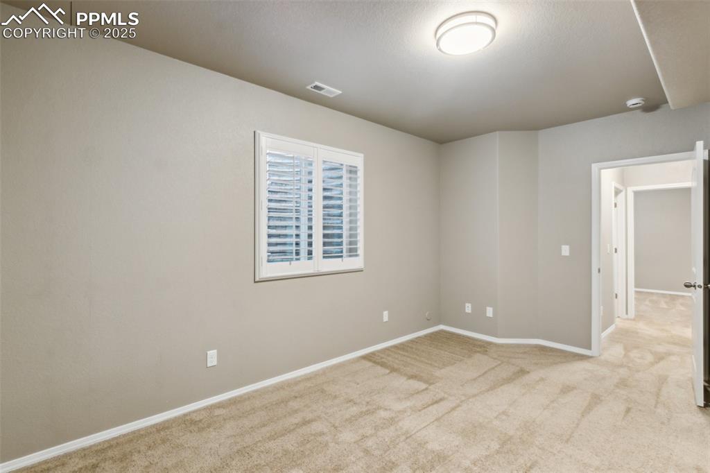 Image 32 of 50: Finished bedroom in lower level with light colored carpet and baseboards