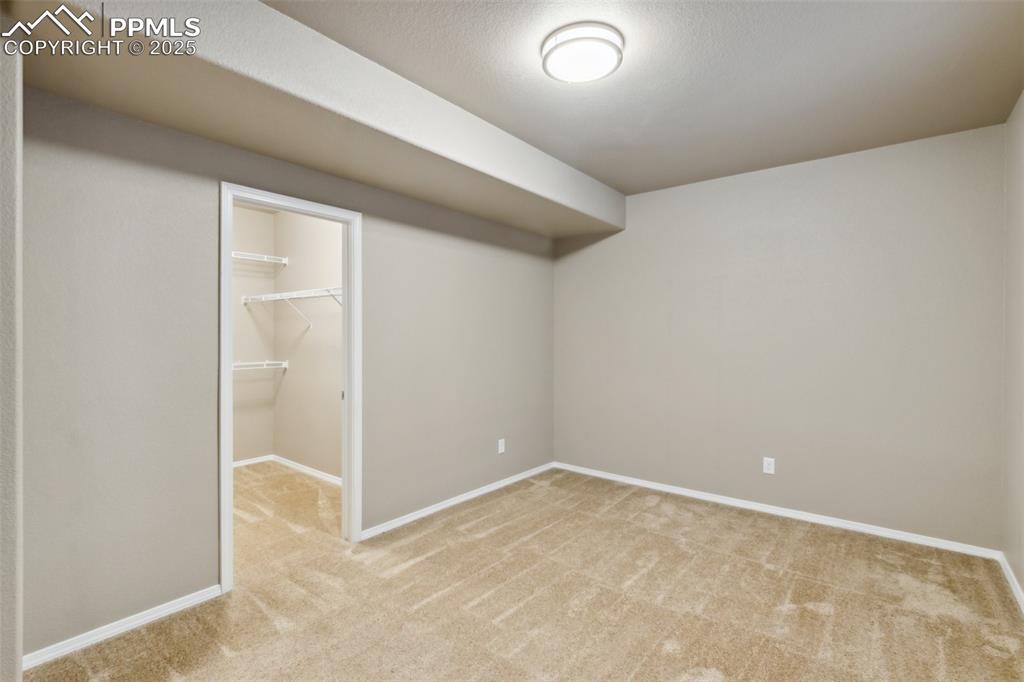 Image 33 of 50: Finished bedroom in lower level with light colored carpet and baseboards