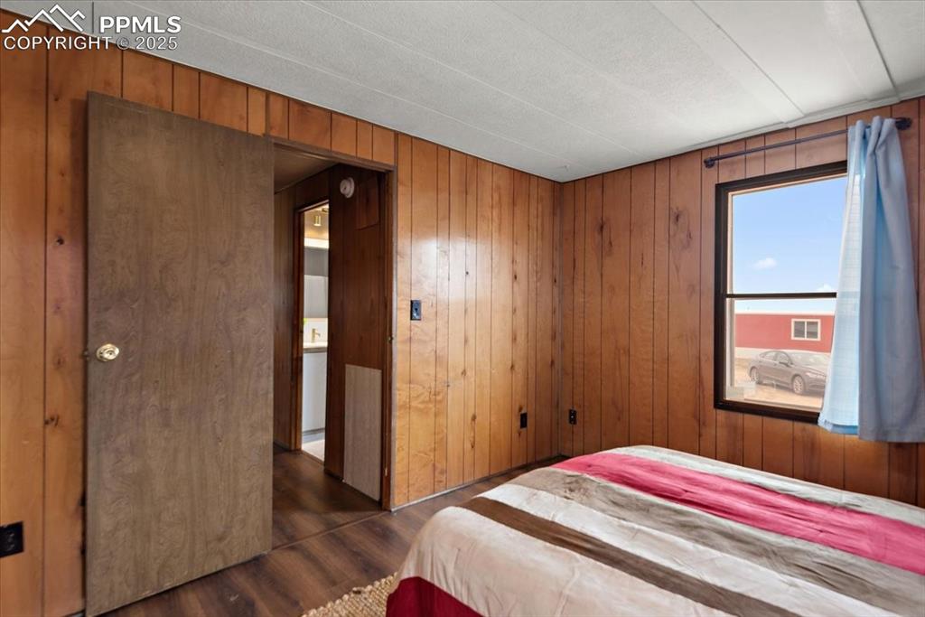 Image 19 of 50: Bedroom featuring wooden walls and dark wood-type flooring