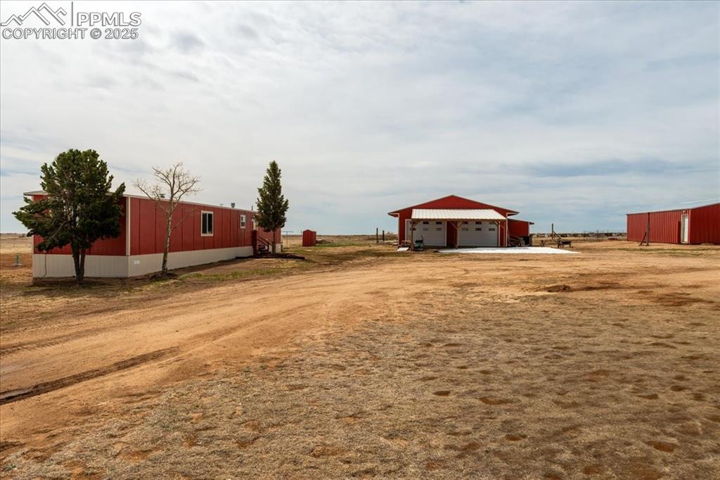 Image 20 of 50: View of yard with dirt driveway, an outbuilding, a garage, and a pole build