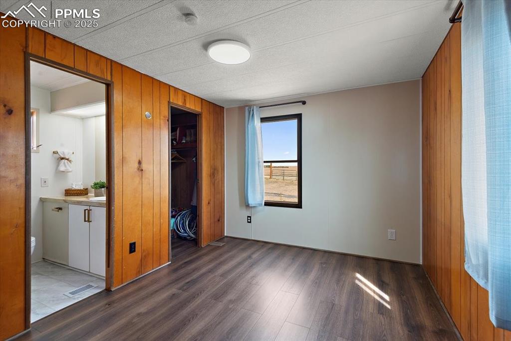 Image 8 of 50: Unfurnished bedroom featuring visible vents, wooden walls, wood finished fl
