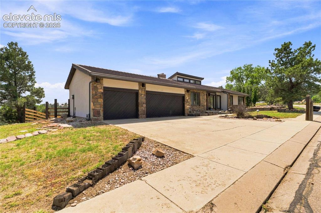 Image 1 of 49: Stone and stucco exterior with multiple garage bays, a paved driveway, and