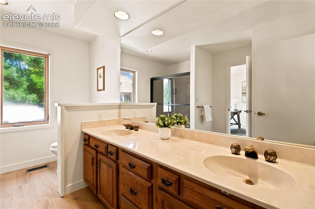Image 15 of 49: Spa-inspired primary bathroom featuring a wood-finish vanity with dual sink