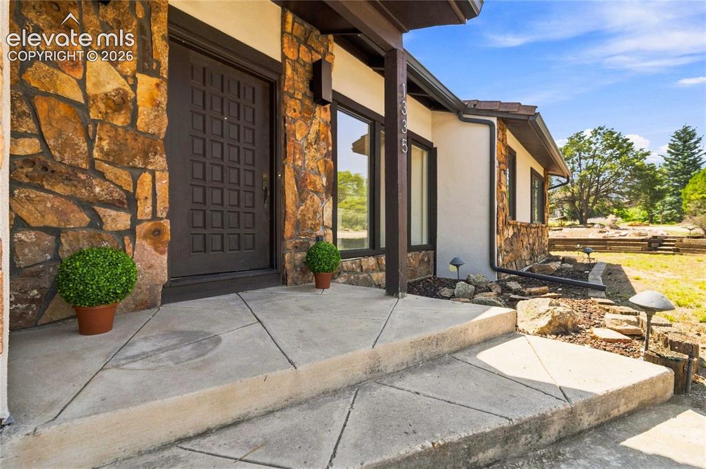 Image 2 of 49: Welcoming entry featuring a rustic stone and stucco exterior with dark wood