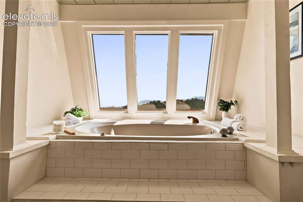 Image 23 of 49: Luxurious soaking tub positioned beneath a triple-window bank offering natu
