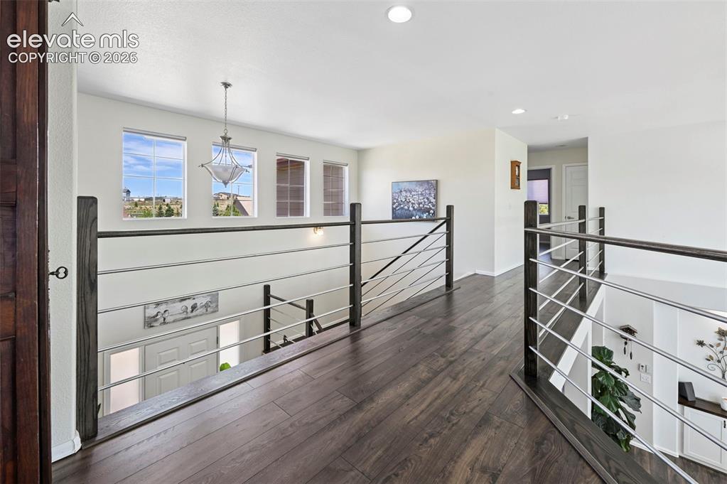 Image 20 of 36: Upper-level hallway featuring dark wood-finish flooring, a contemporary cha