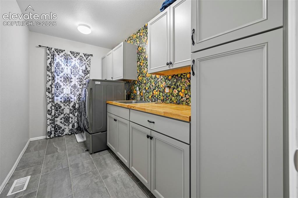 Image 30 of 36: Utility space featuring extensive gray cabinetry and wood-finish countertop