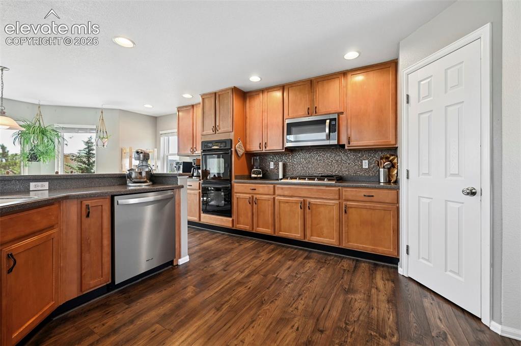 Image 7 of 36: Kitchen featuring wood-finish flooring, warm wood cabinetry, dark counterto