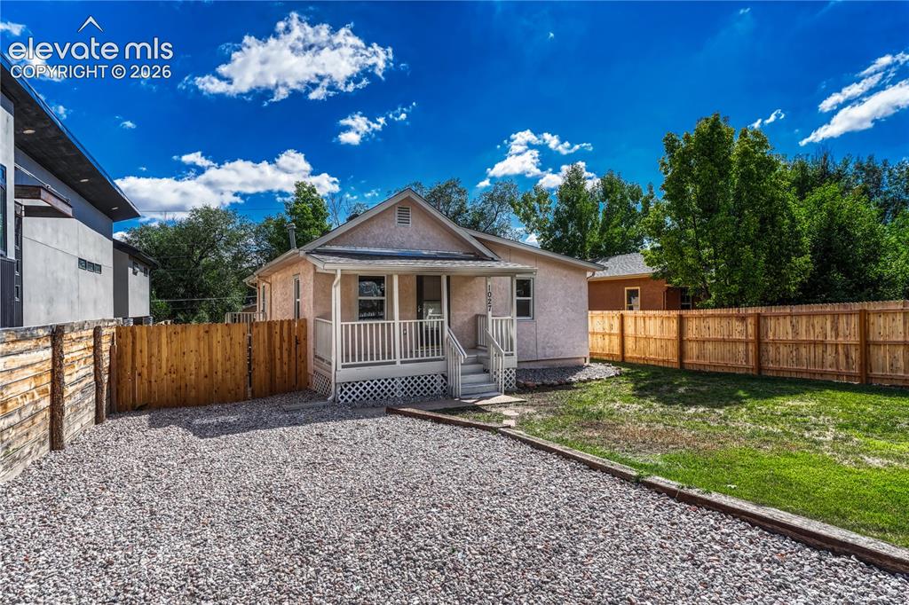 Caption: Gravel parking area, white porch with railings, private wood fencing, and a grassy backyard