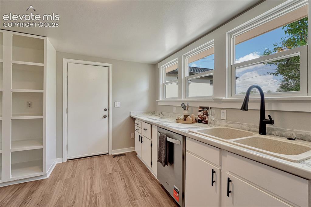 Image 10 of 41: Modern kitchen featuring wood-finish flooring, white cabinetry with black h