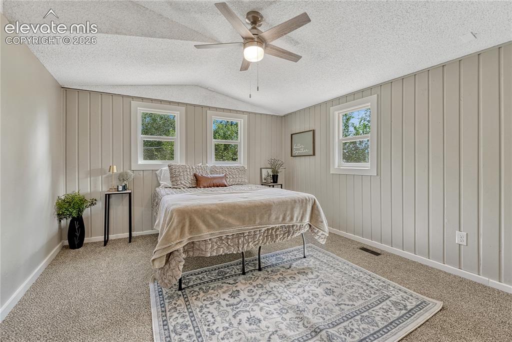 Image 12 of 41: Bright primary bedroom featuring vertical shiplap accent walls, multiple wi