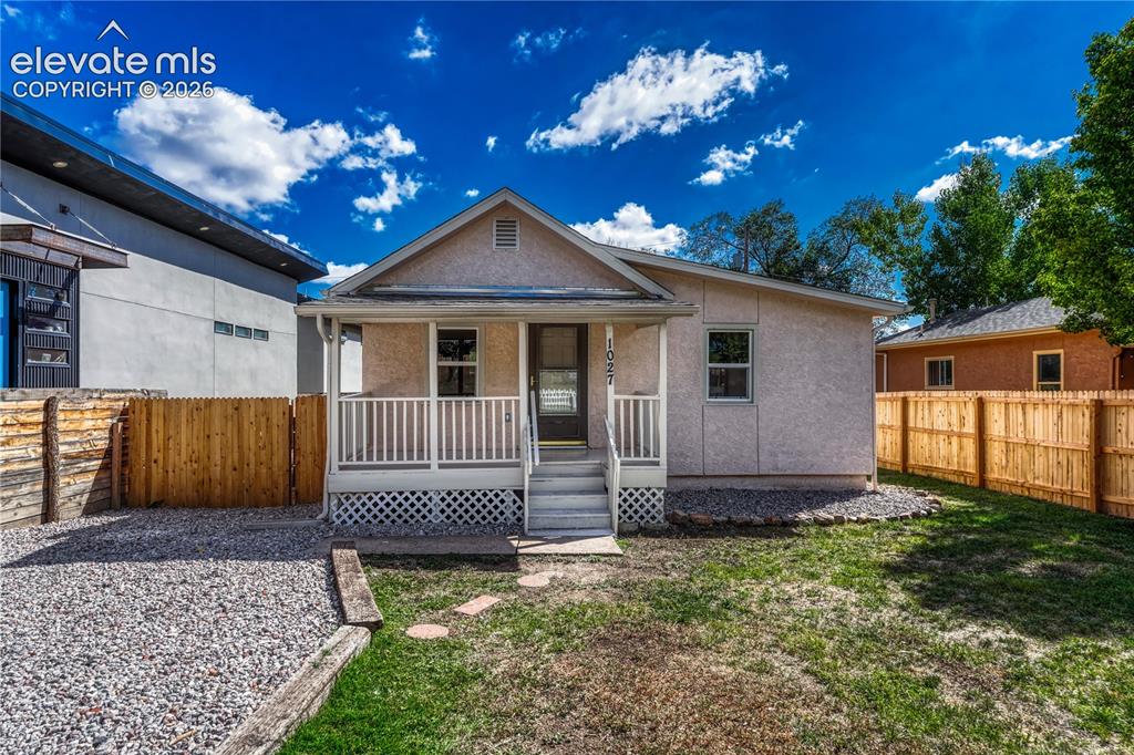 Image 2 of 41: Stucco exterior with a covered porch, white railing, and a gravel driveway