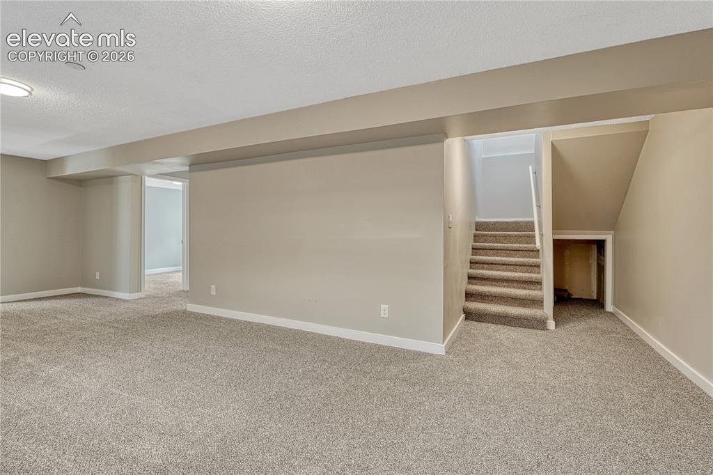 Image 22 of 41: Expansive carpeted area with neutral wall tones and a stairway featuring a 