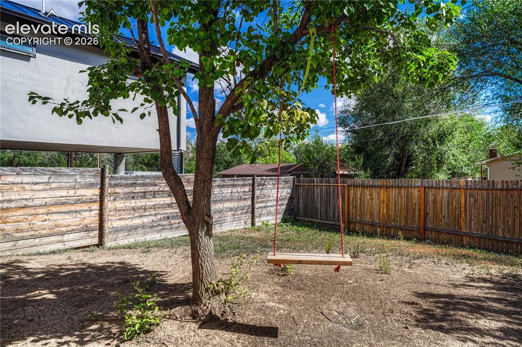 Image 31 of 41: Expansive backyard with a mature tree, wood plank fencing, and partial stuc