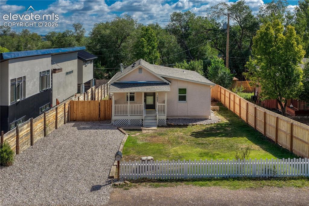 Image 34 of 41: Gravel driveway, white picket fence, covered front porch, and expansive law