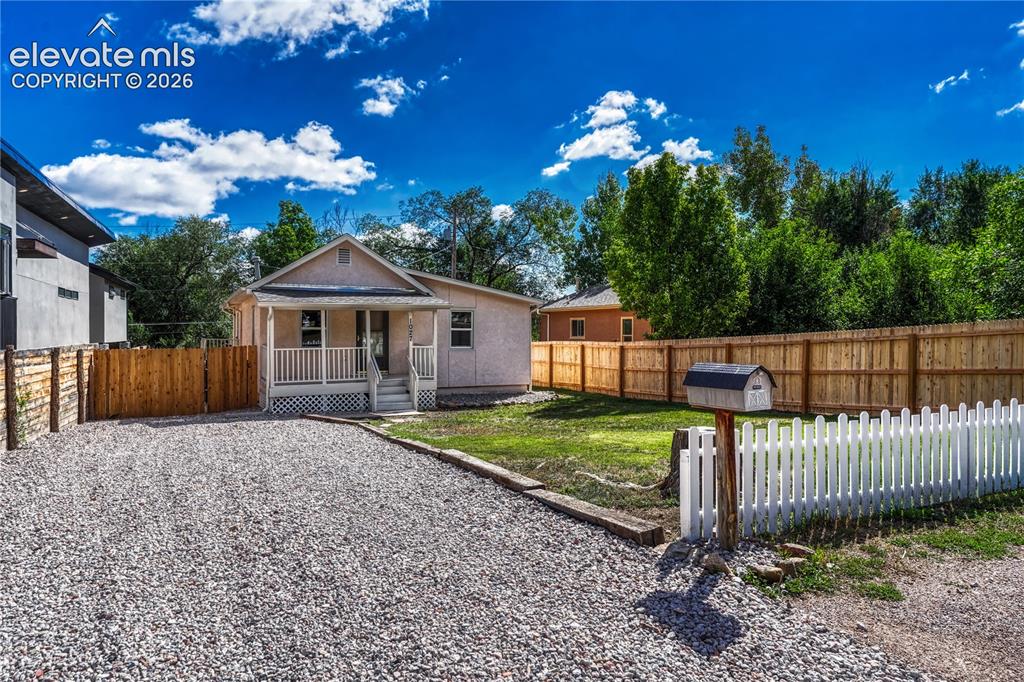 Image 36 of 41: Gravel driveway with a white picket fence, wood privacy fencing, and a fron