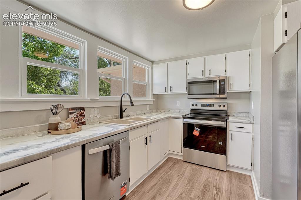 Image 8 of 41: Kitchen featuring white cabinetry, light-toned countertops, wood-finish flo
