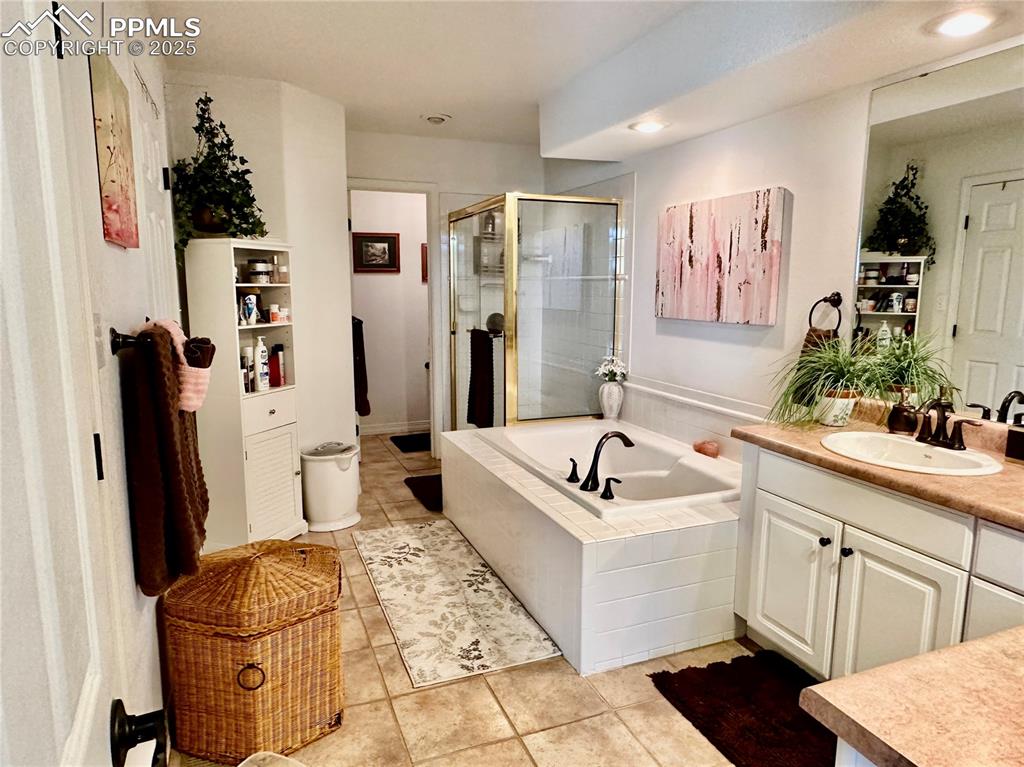 Image 12 of 41: Bathroom with vanity, light tile patterned floors, a bath, and a stall show
